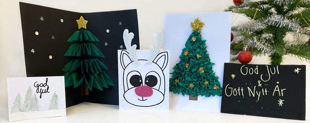 Närbild av en julgran med röda glittriga kulor och ett kort med texten 'God Jul' framför snötäckta träd